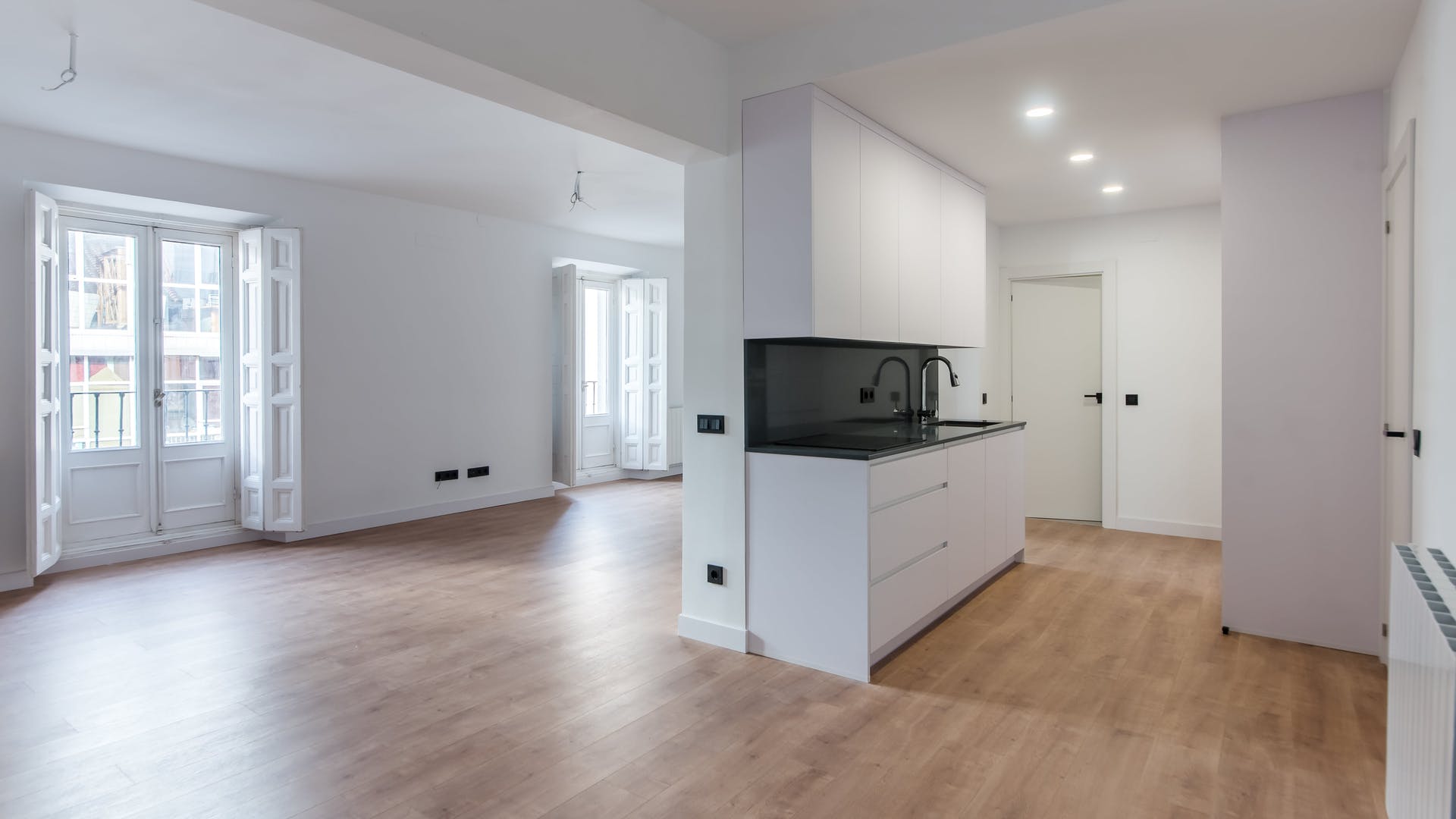 Salón moderno con cocina americana y ventanas blancas.