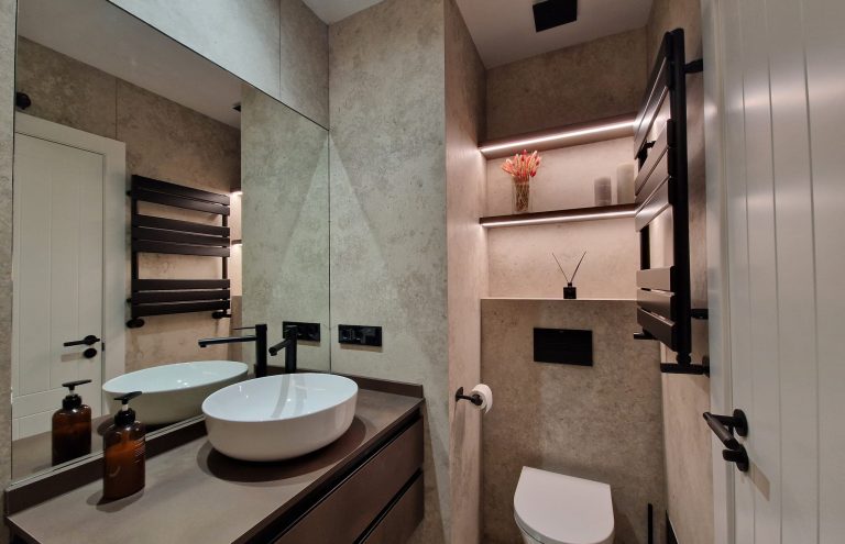 Baño moderno con azulejos beige, inodoro y lavabo blanco.
