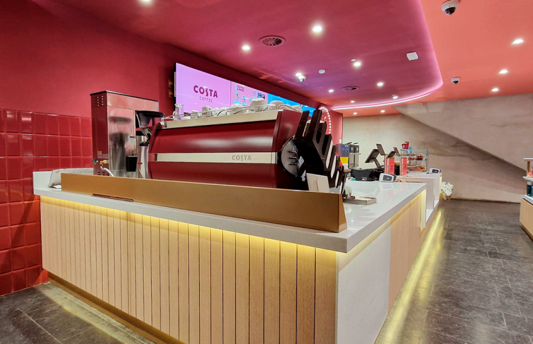 Mostrador de cafetería Costa Coffee con diseño moderno y luces.