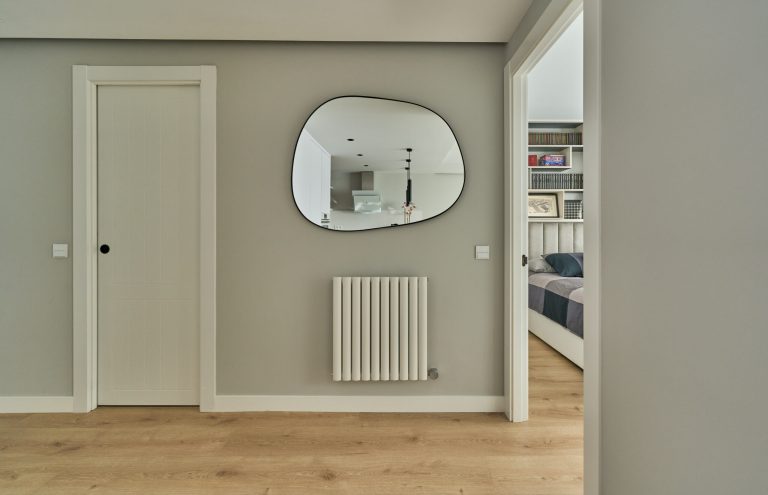 Pasillo moderno con espejo ovalado y radiador blanco.