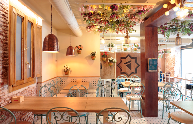 Interior de cafetería decorada con flores y ladrillo visto.