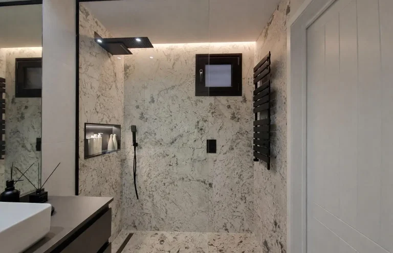 Ducha moderna con revestimiento de mármol y toallero negro.